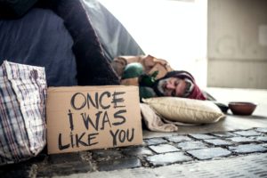 Homeless beggar man lying on the ground outdoors in city, sleeping.