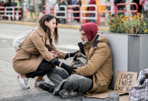 Young woman giving money to homeless beggar man sitting in city.